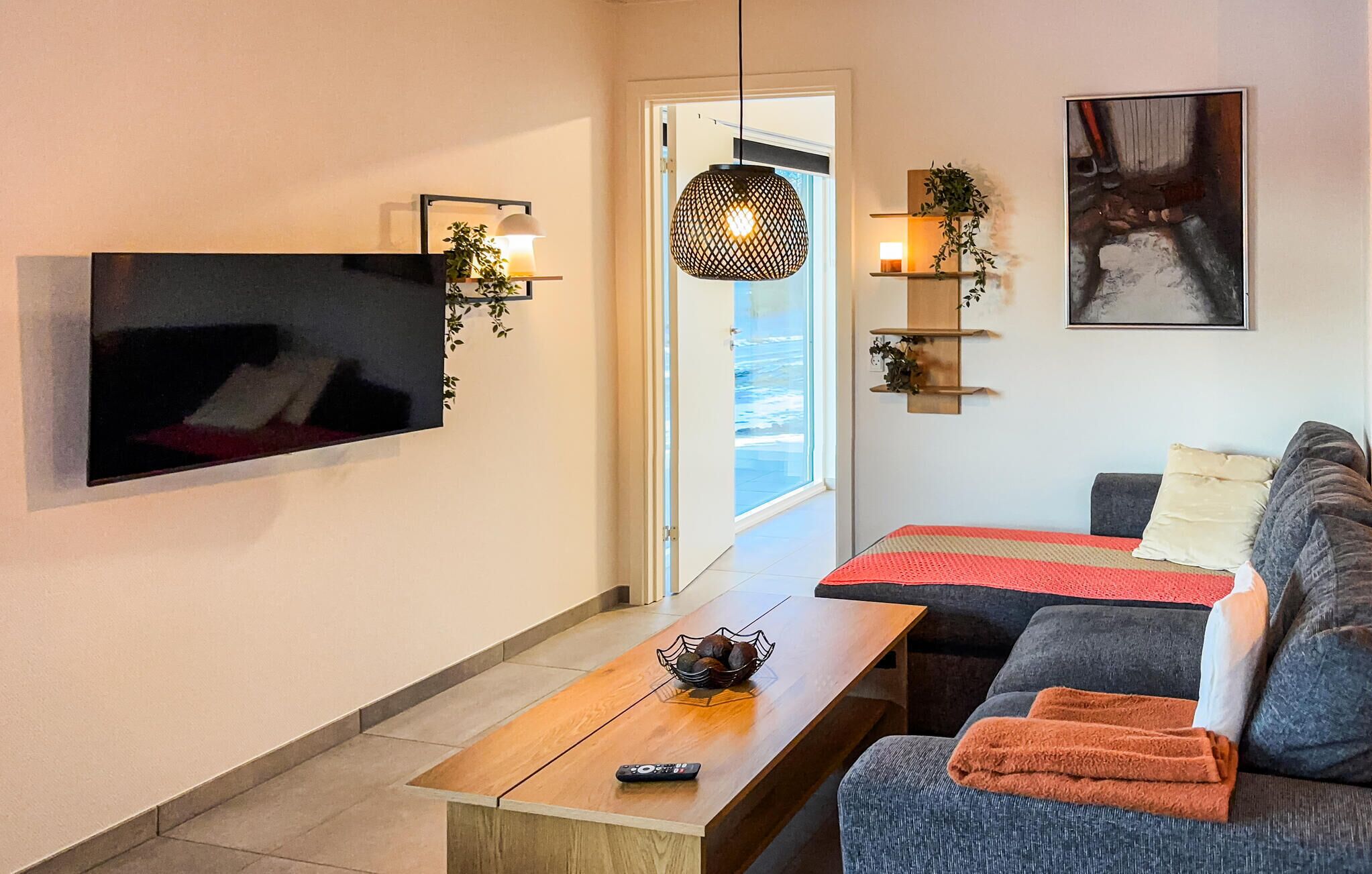Una sala de estar moderna con un televisor de pantalla plana montado en la pared, una mesa de centro de madera, un sofá gris y una manta roja.