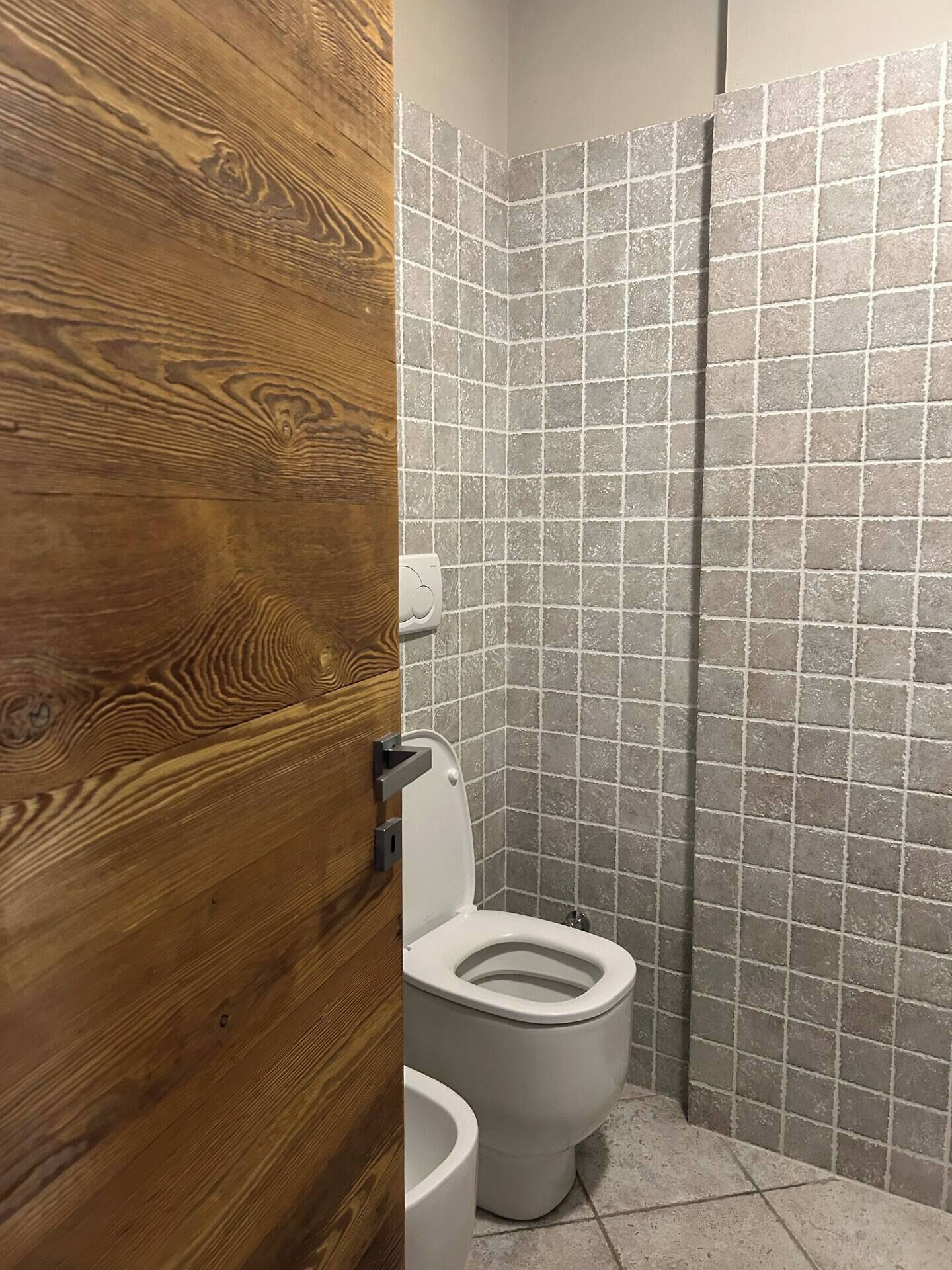 Ein Badezimmer mit einem Holzbadezimmer-Möbel, einer weißen Toilette und einem gefliesten Duschbereich.