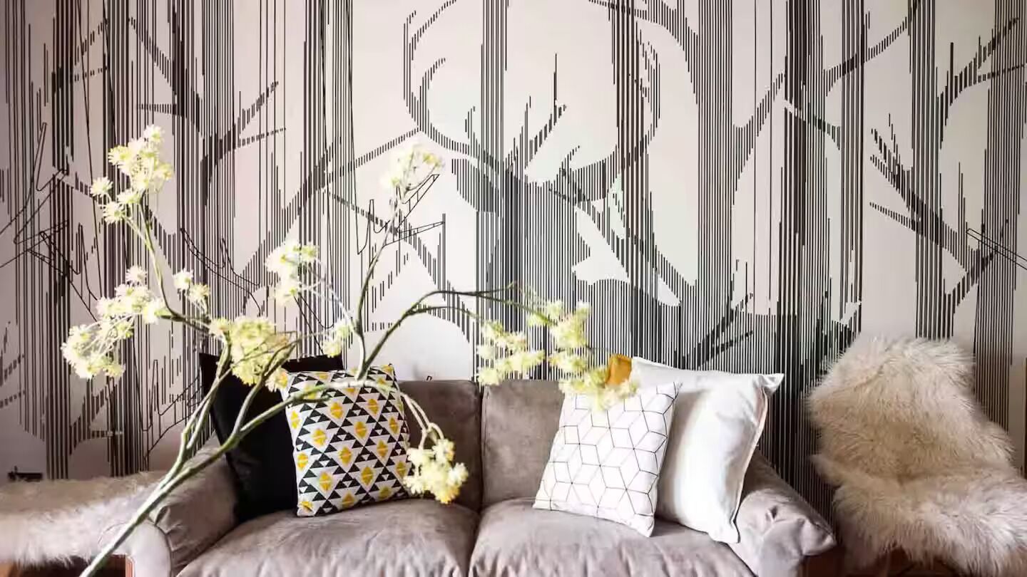 Ein Sofa mit gemusterten Kissen und eine Blumenvase vor einer Wand mit vertikalen Linien.