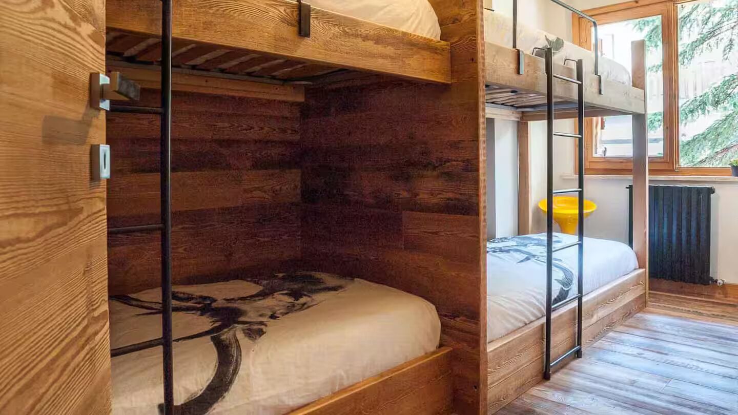 Ein Schlafraum mit Etagenbetten, Holzboden und einem Fenster mit Blick auf Bäume.