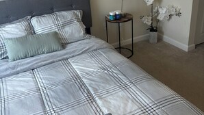 A neatly made bed with a checkered bedspread, a grey headboard, and a bedside table with a lamp and a vase of white flowers. - Cozy 1-bedroom apartment in beautiful Vienna with AC and gym access (Vienna)