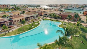 A large, curved swimming pool surrounded by palm trees and a view of the sea. - TAN Residences at Fishing Lodge (Punta Cana)