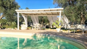 A clear swimming pool with a pergola and outdoor seating.