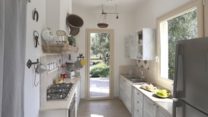 A kitchen with a gas stove, sink, and refrigerator, a window with a view of greenery, and a door leading to an outdoor area.