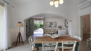 A dining area with a wooden table, white chairs, a lamp, and a view of the outdoors.