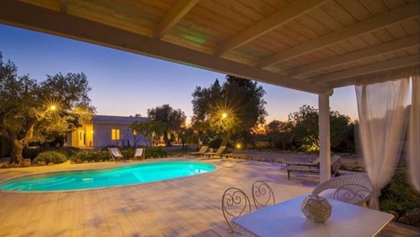 A swimming pool with lounge chairs and a table under a covered area.