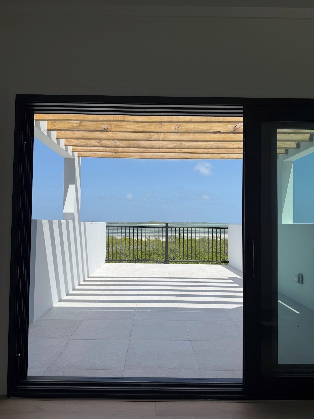 A modern balcony with a wooden pergola, a metal railing, and a clear view of the sea.