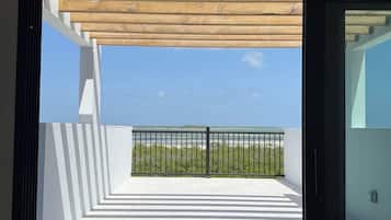 A modern balcony with a wooden pergola, a metal railing, and a clear view of the sea.