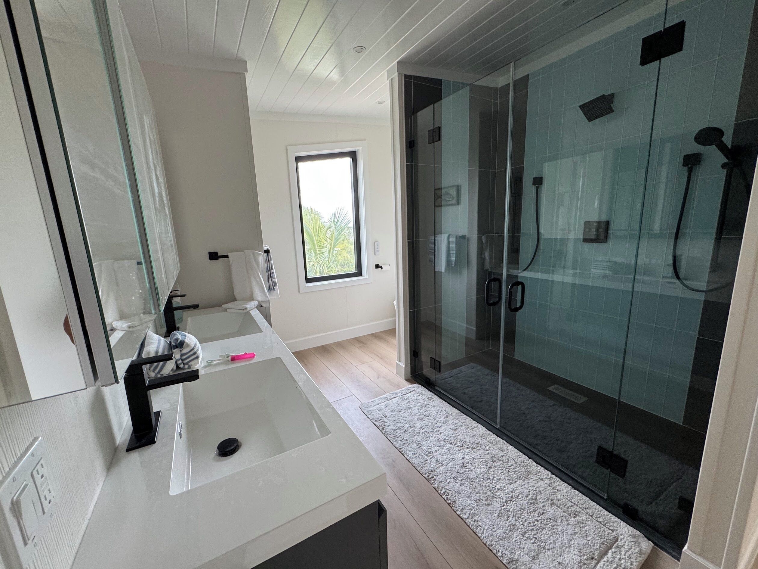 Une salle de bain moderne avec une douche à parois de verre, un lavabo blanc et une fenêtre laissant entrer la lumière naturelle.