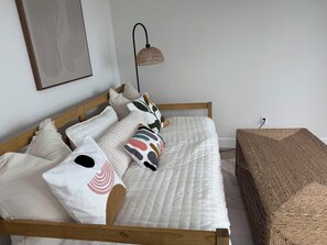 A neatly made bed with a white quilt, multiple pillows, and a woven bench beside it.