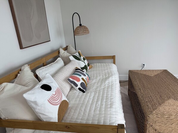 A neatly made bed with a white quilt, multiple pillows, and a woven bench beside it. - Coastal Casuarina Sanctuary Nestled on the Water's Edge (Central Abaco)