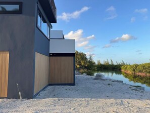 Un bâtiment moderne doté d’un toit plat, de grandes fenêtres et offrant une vue sur une étendue d’eau paisible et une végétation luxuriante.