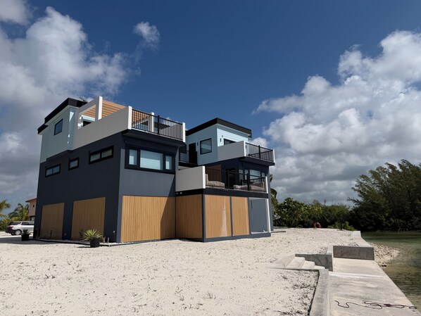 A modern multi-story building with a flat roof, large windows, and a balcony. - Coastal Casuarina Sanctuary Nestled on the Water's Edge (Central Abaco)