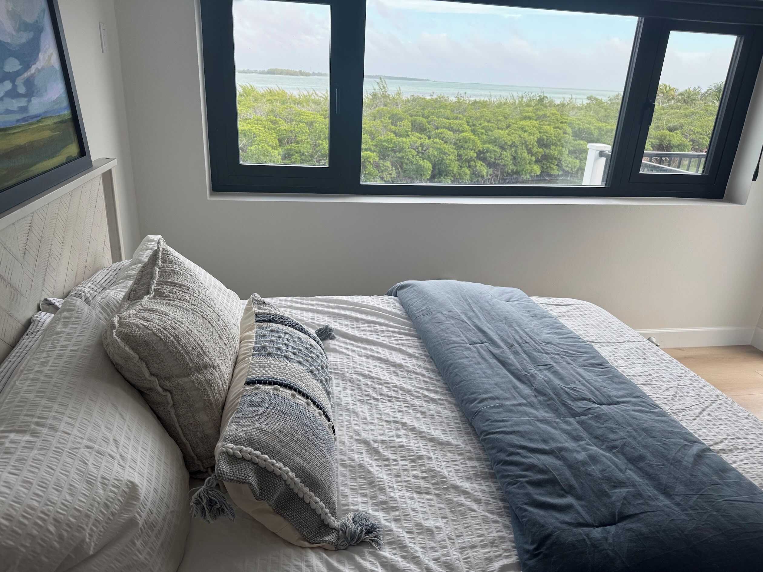 A bedroom with a large window offering a view of a coastal landscape.
