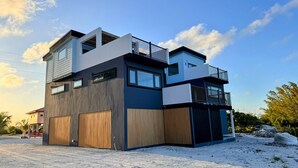 Une maison moderne à deux étages, dotée d’un garage, de grandes fenêtres et d’un balcon.