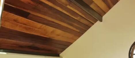 Un dormitorio con cama, una mesa con un florero, un calentador negro y un techo de madera.