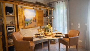 A dining area with a round table set for two, surrounded by leather chairs. A painting and wooden shelves with various items are visible in the background. - Exclusive vacation home with private barrel sauna - peace & nature (Beelitz)