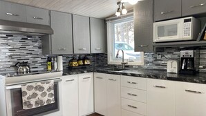 Una cucina moderna con mobili bianchi, una cappa in acciaio inossidabile, un forno a microonde, un tostapane e una macchina da caffè.