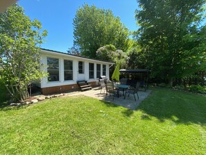 Et hus med terrasse, overdækket siddeområde og græsplæne.