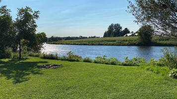 A grassy area with a river, trees, and a clear sky.
