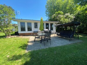 En terrasse med et bord og stole, en gyngestol og et overdækket siddeområde.