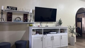 Ett vardagsrum med en platt-TV som är monterad på väggen, ett vitt TV-bord under och två blå sittpallar.