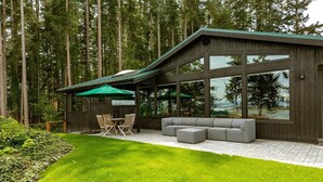 Una casa moderna con un porche cubierto, un comedor y un gran ventanal con vista a un bosque.