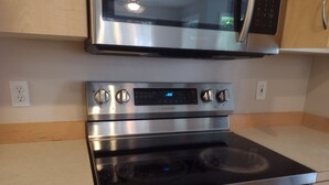 Un horno de acero inoxidable con pantalla digital, un microondas encima y armarios de madera.