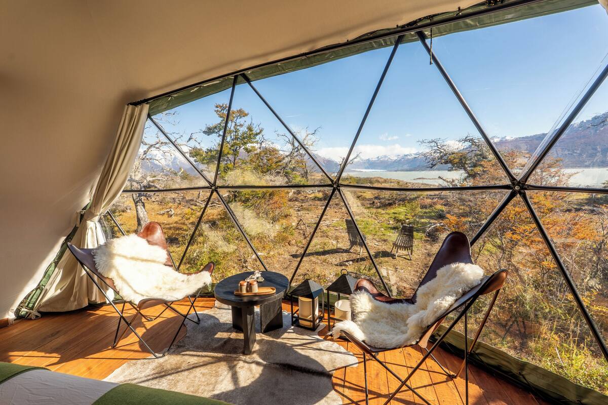 Ein Raum in Form einer Geodätischen Kuppel mit zwei Sesseln, einem kleinen Tisch und Blick auf eine Berglandschaft.