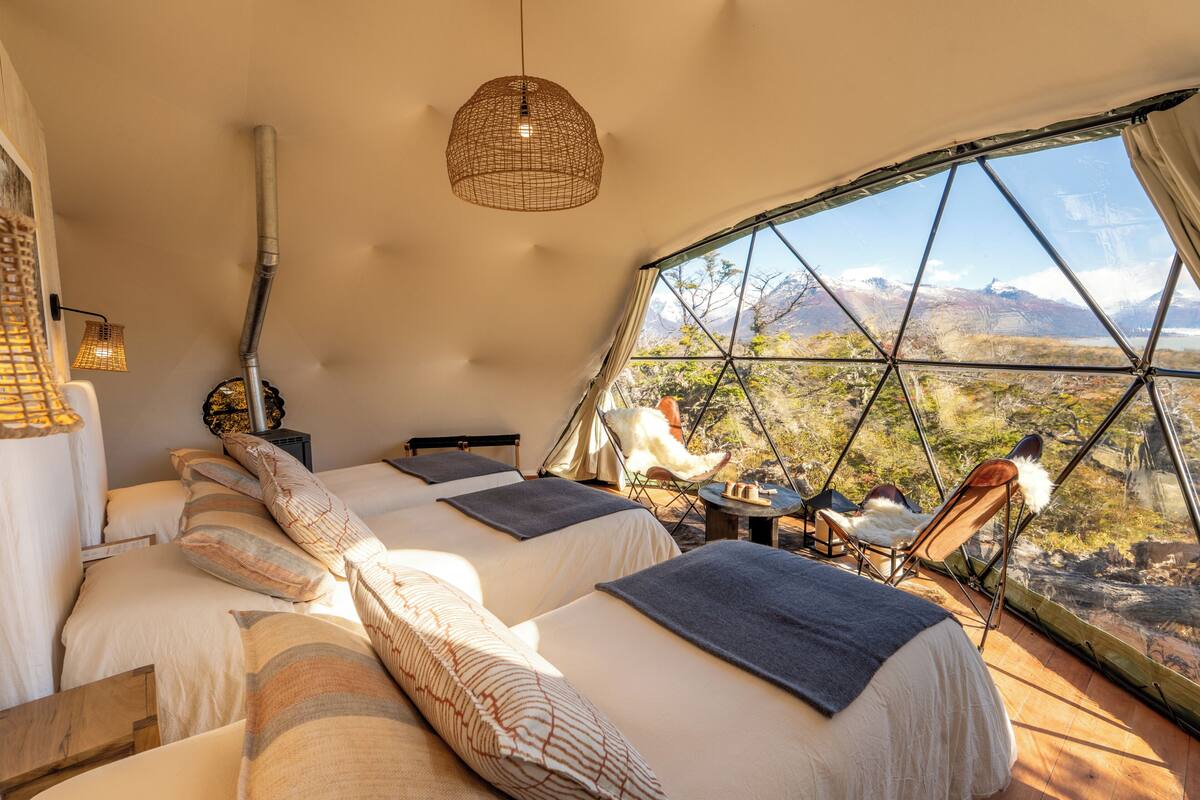 Eine Zelthütte mit drei Betten, einer Hängelampe und Blick auf eine Berglandschaft.