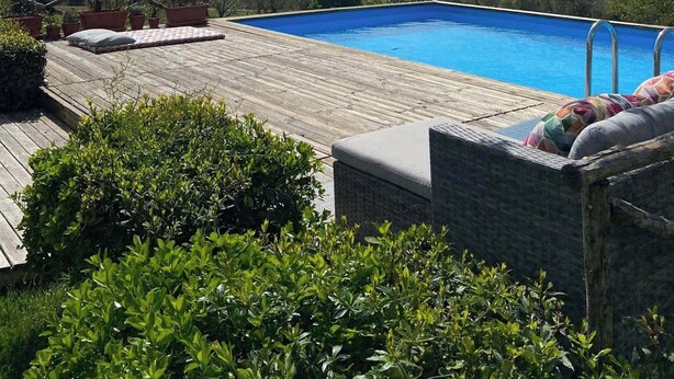 Μια πισίνα με ξύλινο δάπεδο και ξαπλώστρες, περιτριγυρισμένη από πράσινο και με θέα σε ένα πανέμορφο τοπίο.