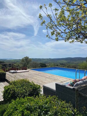 A swimming pool with a wooden deck and lounge chairs, surrounded by greenery and overlooking a scenic landscape. - Tenuta Le Mandorlaie Agriturismo (Scansano)