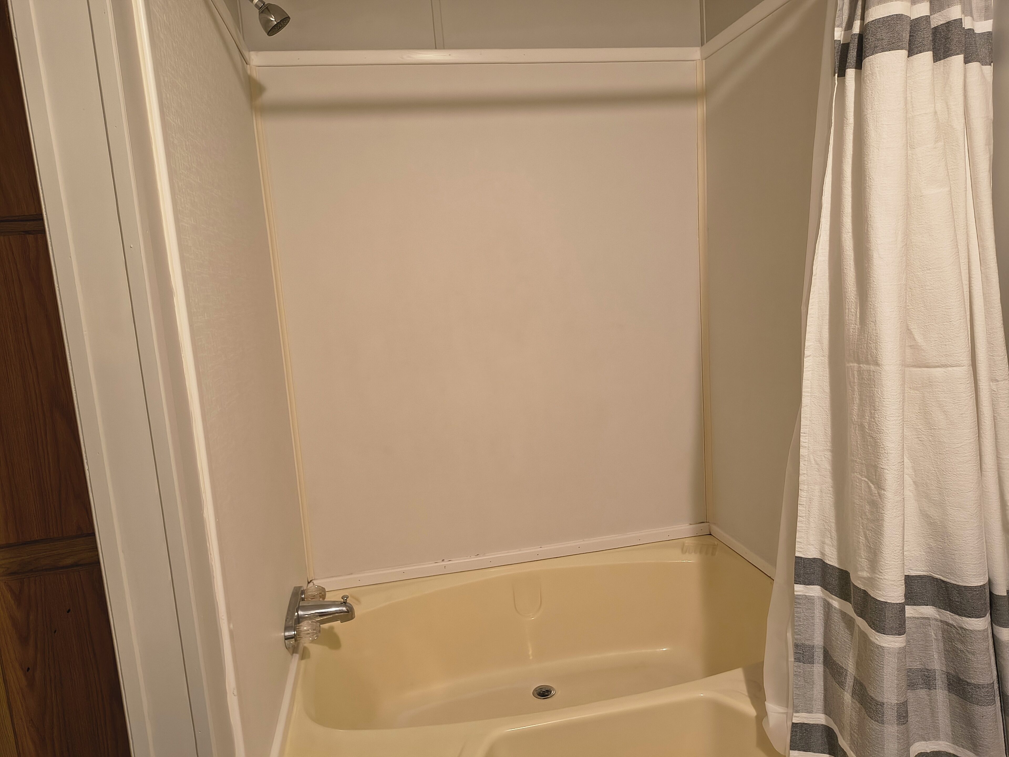 A corner bathroom with a bathtub, a shower curtain, and a wooden door.