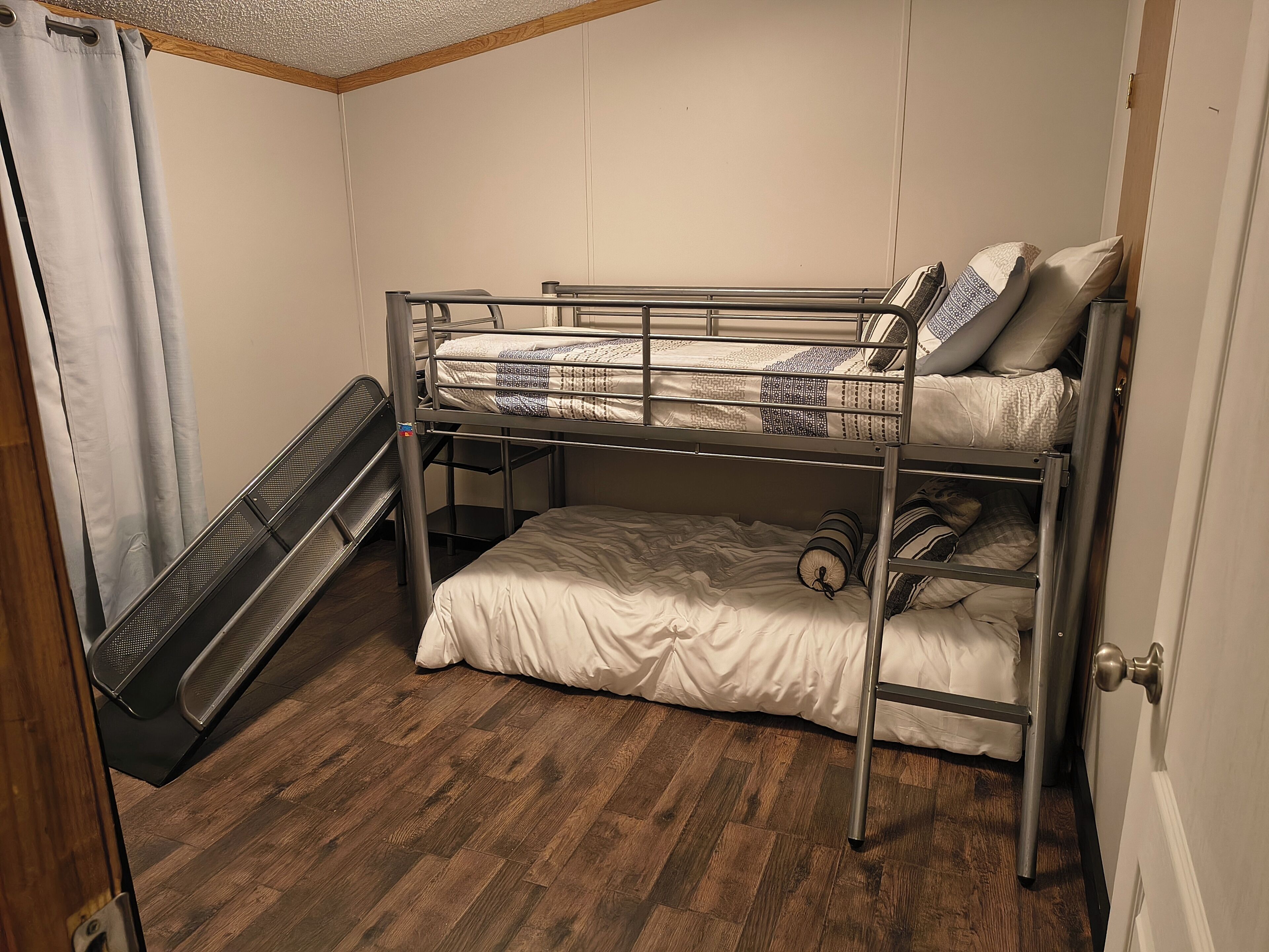A bunk bed room with a metal ladder, a pull-up bar, and a window with curtains.