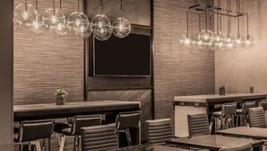 A modern hotel lobby with a bar area, seating, and a large flat-screen TV mounted on the wall.