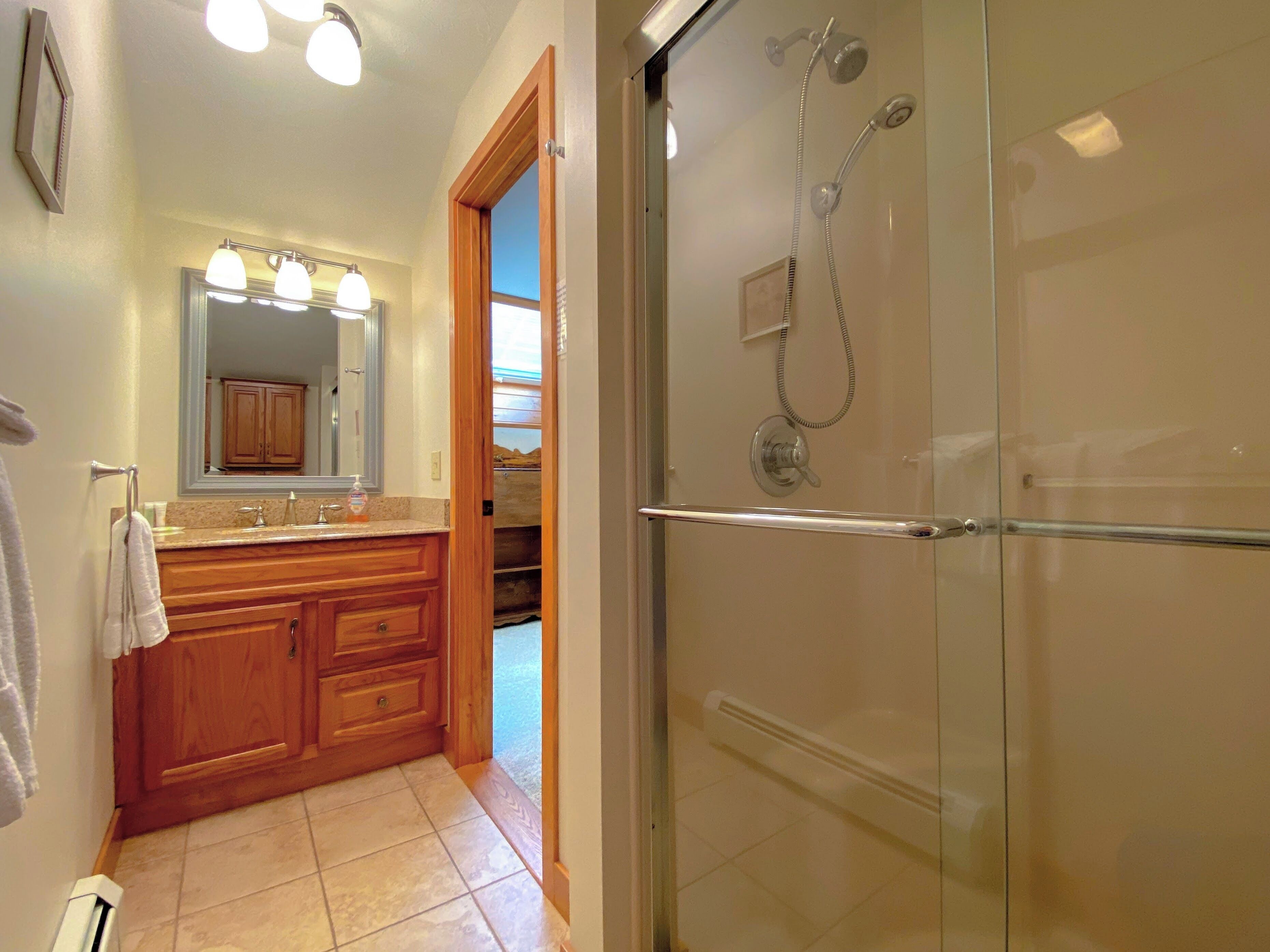 A bathroom with a glass shower enclosure, wooden vanity, and a large mirror.
