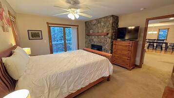 Un dormitorio con cama, cómoda, televisor, chimenea y balcón con vista a árboles.