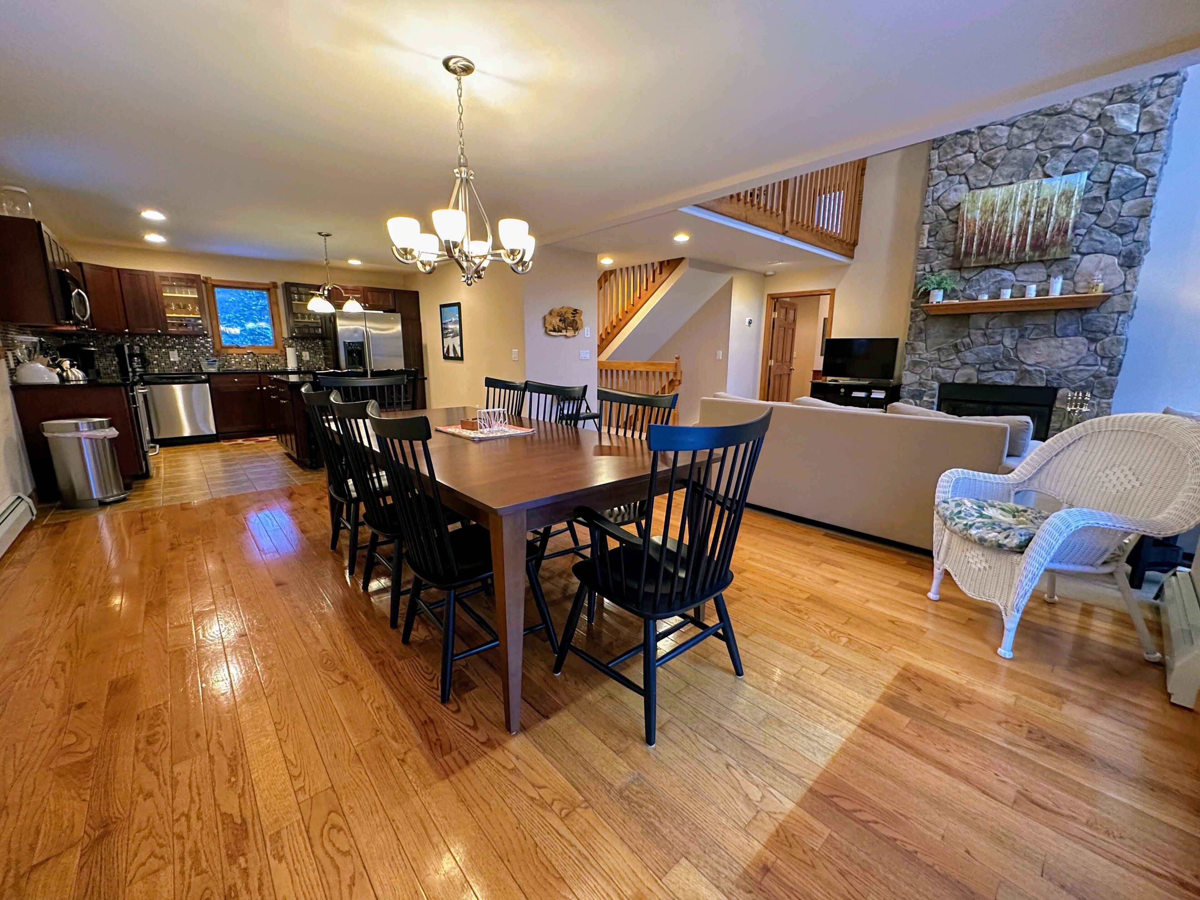A spacious kitchen with wooden flooring, a dining area with a table and chairs, a living room with a sofa and a television, and a stone fireplace.