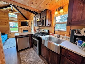A compact kitchen with a stove, microwave, and sink. - Bmv8 Tiny Home Topline (Twin Mountain)
