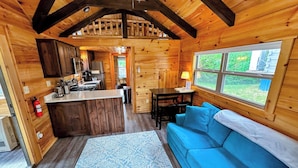 Interior de una cabaña con cocina, comedor y un sofá azul.