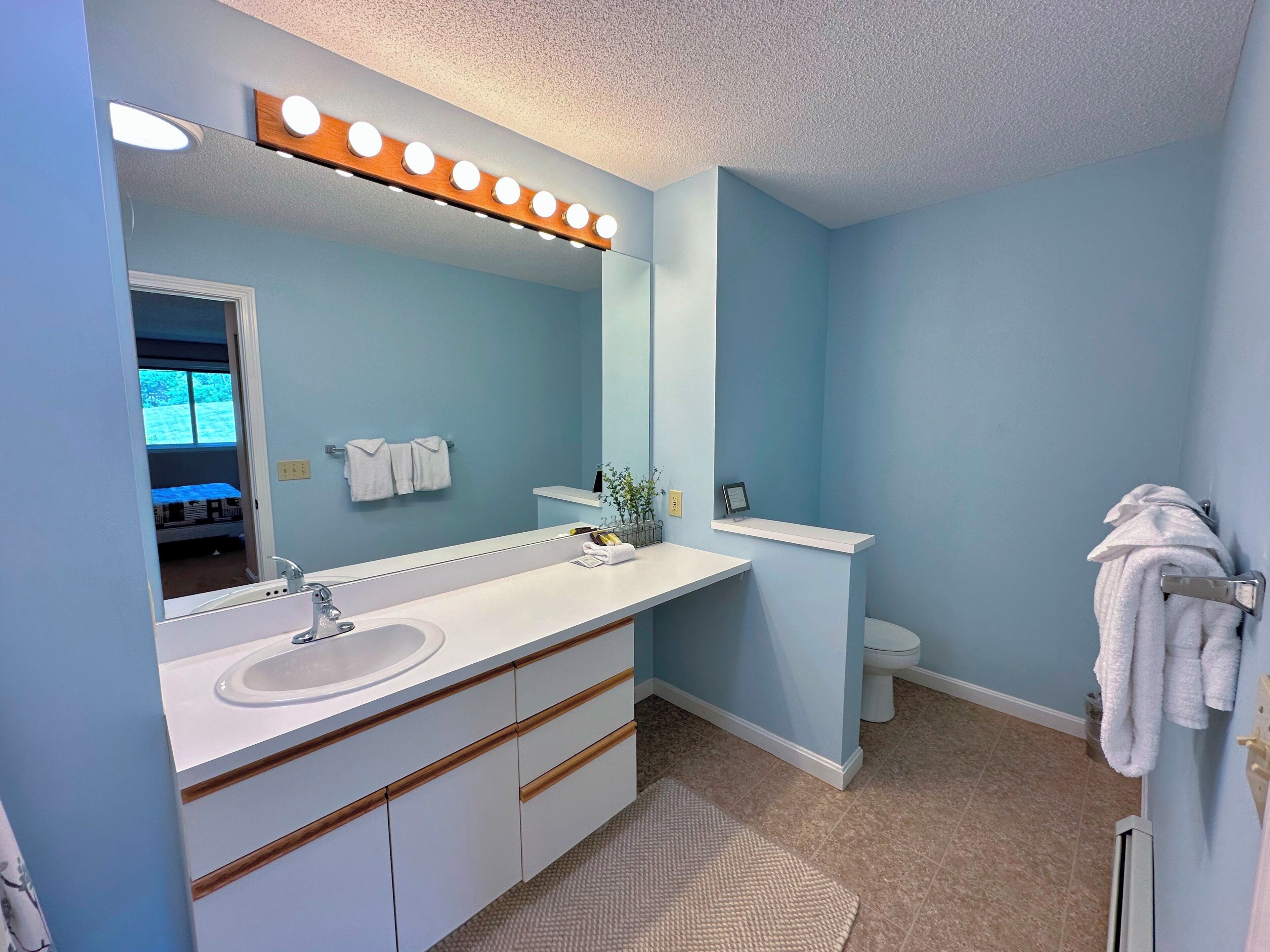 A bathroom with a white vanity, a large mirror, and a lighted vanity mirror.