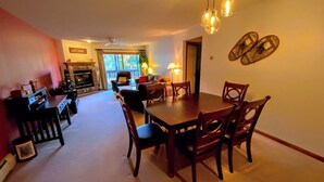Ein geräumiges Wohnzimmer mit Kamin, eine Essecke mit Holztisch und -stühlen und ein Blick ins Freie durch große Fenster.