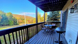 Eine Holzterrasse mit Tisch und Stühlen, mit Blick auf ein bewaldetes Gebiet und Hügel.