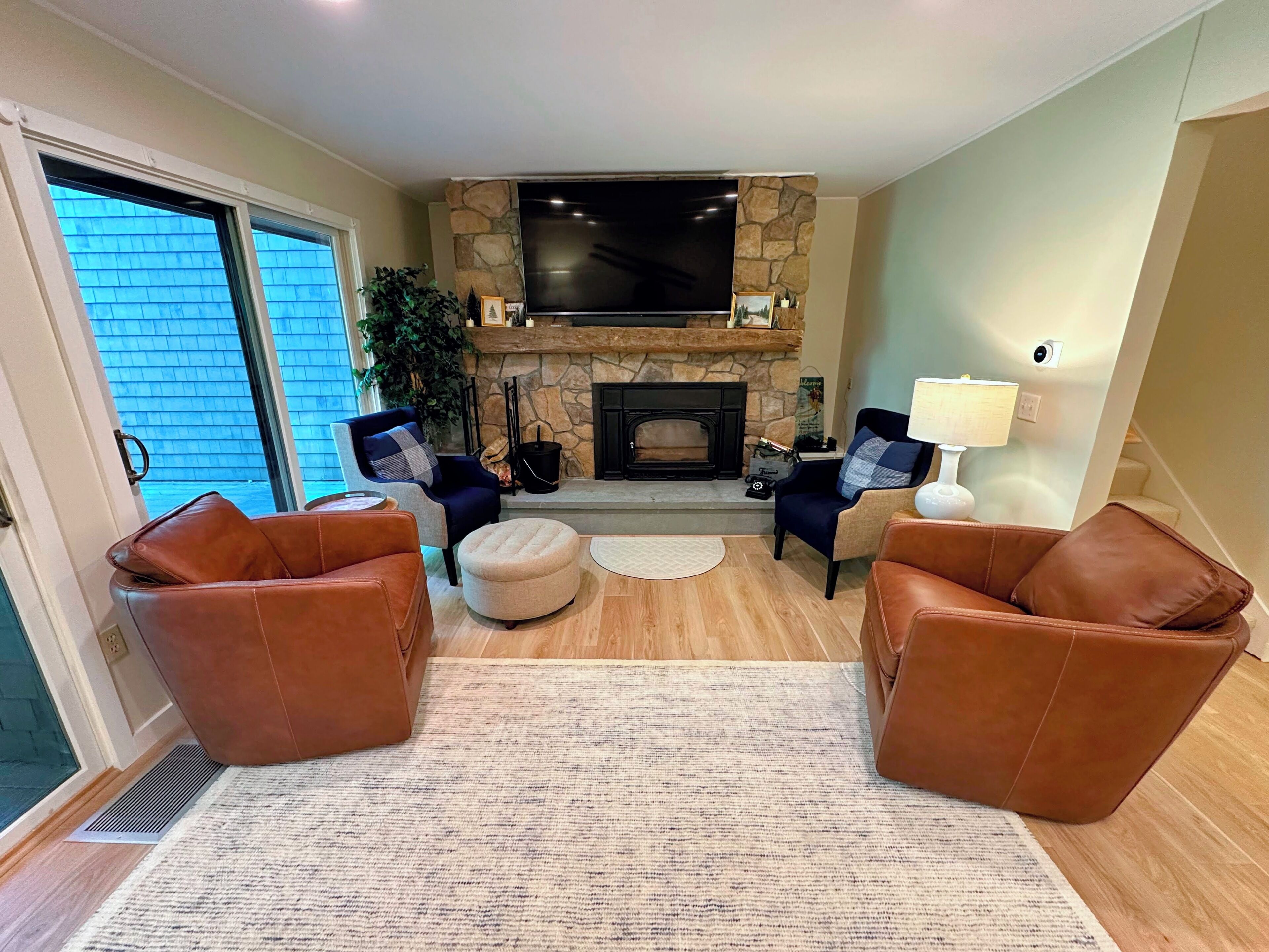 A living room with a stone fireplace, a flat-screen TV, leather sofas, and a large window.
