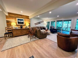 Una sala de estar moderna con una pared de acento de madera, un sofá, sillones, una mesa de centro y vistas al exterior a través de amplios ventanales correderas.