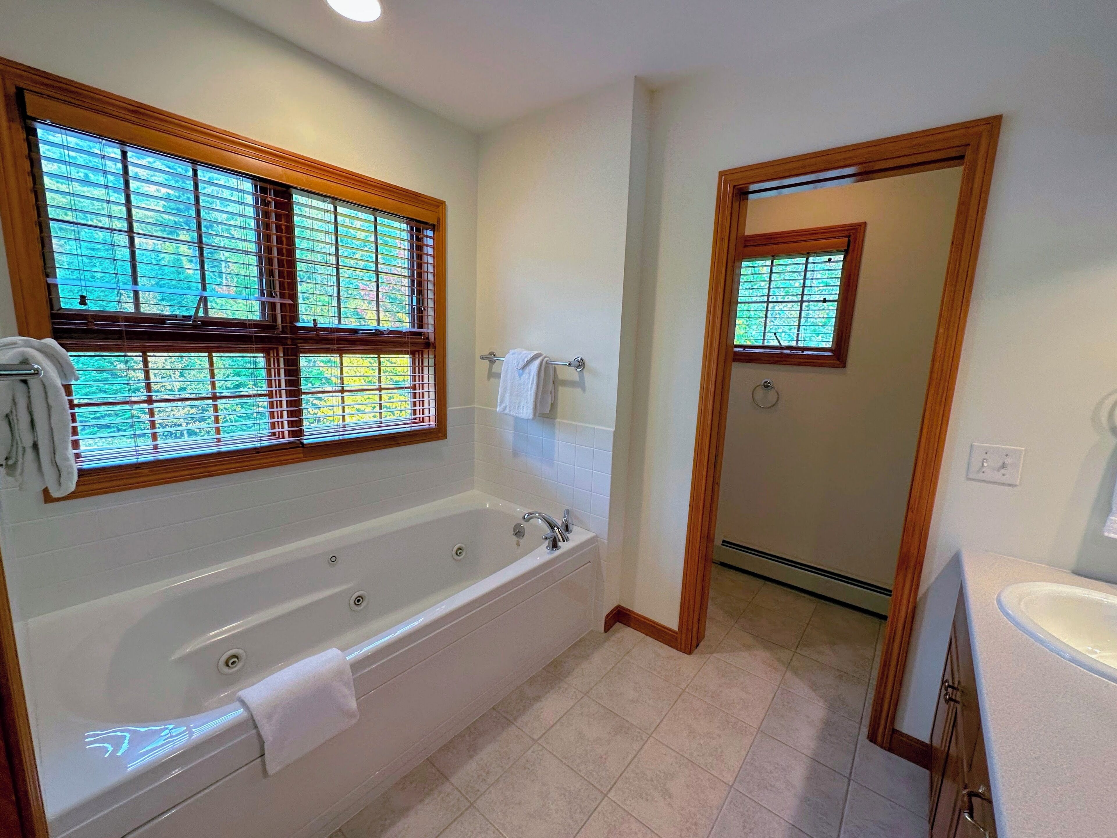 A bathroom with a bathtub, a window with blinds, a towel rack, and a mirror.