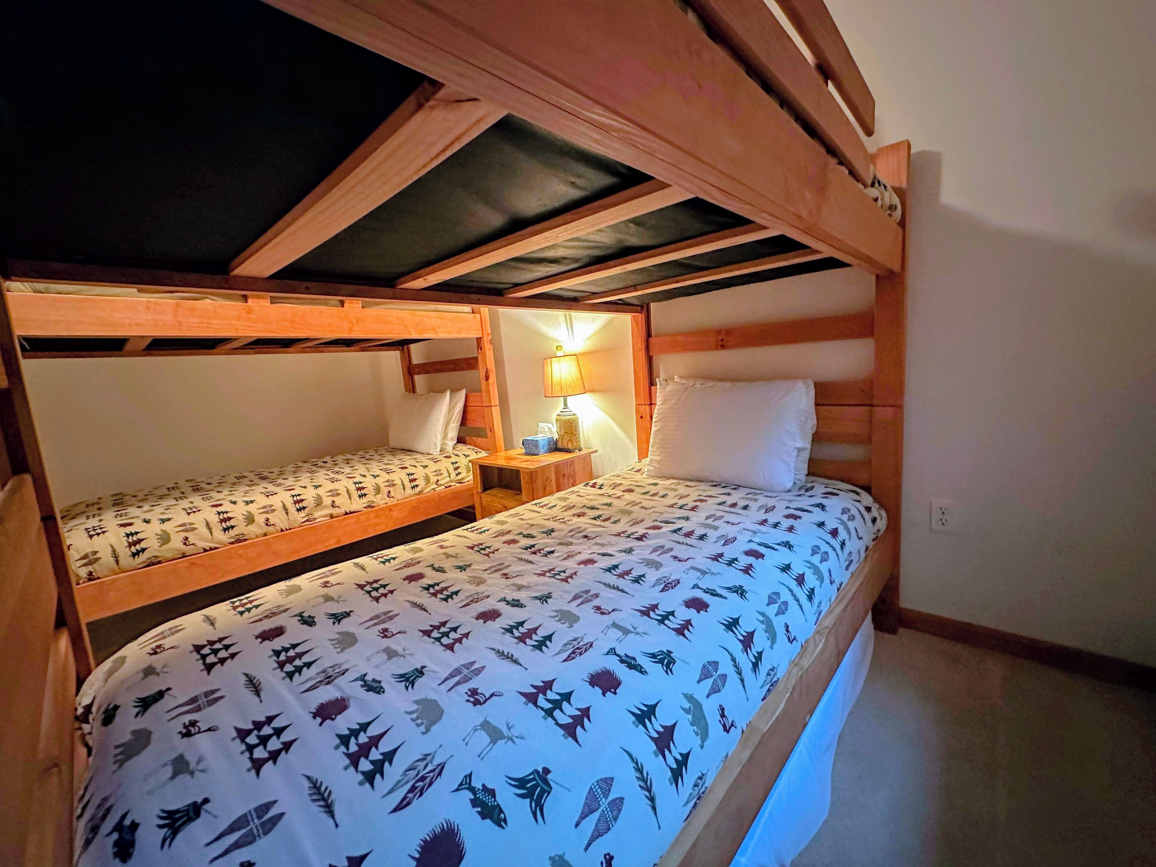 Ein Zimmer mit zwei Etagenbetten, einem Nachttisch mit Lampe und einem Fenster mit Blick zum Himmel.