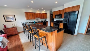 A modern kitchen with wooden cabinets, a central island with bar stools, a black refrigerator, and a microwave. - SH1 Beautiful Stonehill Townhouse in Bretton Woods (Bretton Woods)