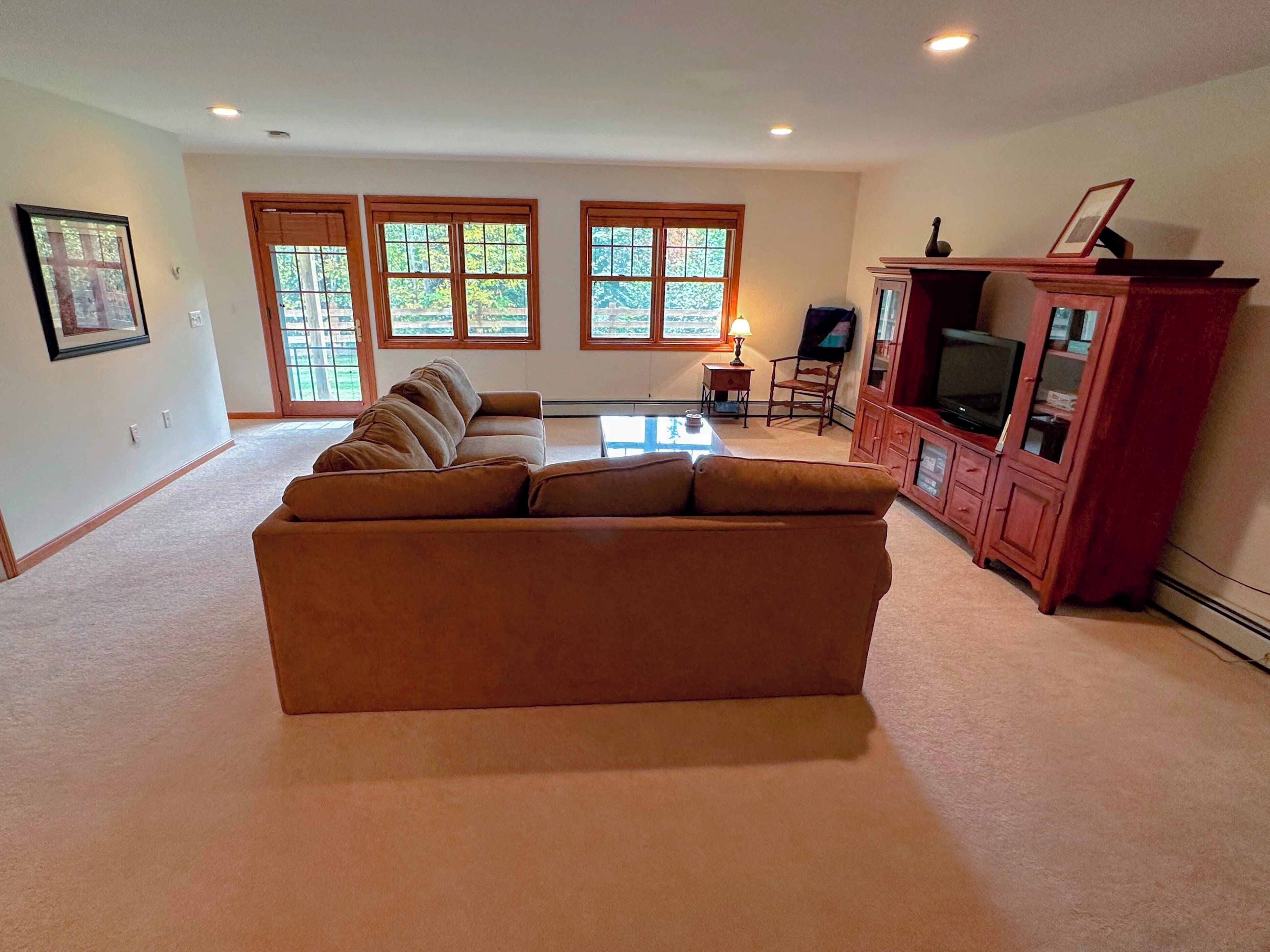 A living room with a sectional sofa, a TV cabinet, and large windows.