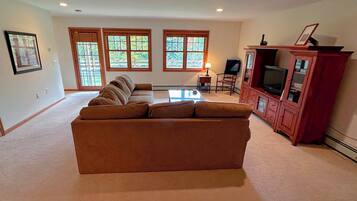 A living room with a sectional sofa, a TV cabinet, and large windows.